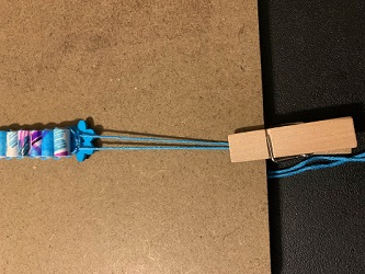 clothespin securing floss to clipboard so knot dries away from bead